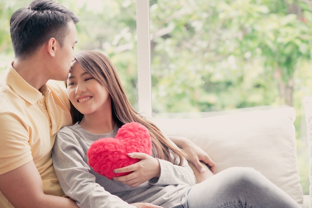 Asian Couples Sitting on the sofa In which women Holding a red heart And smiling happily.