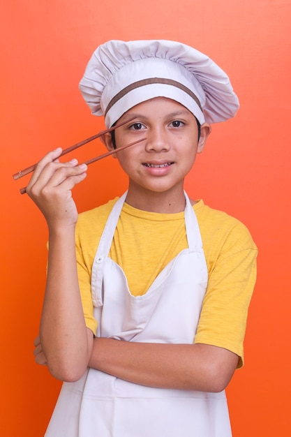 Asian cuisine Adorable little boy in chef uniform holding chopsticks on orange background