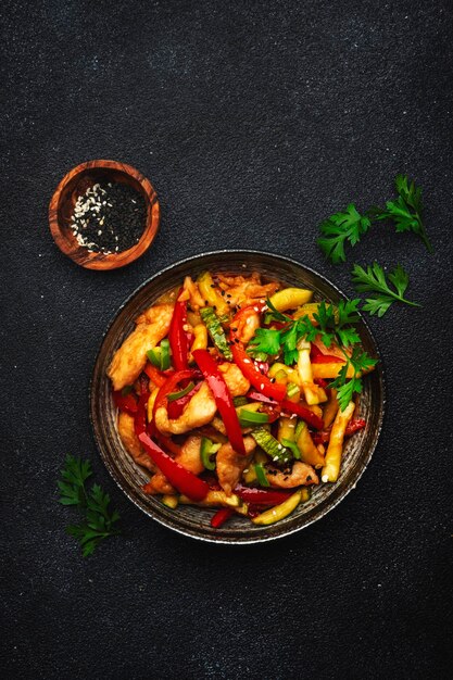 Asian cuisine stir fry with chicken red paprika pepper and zucchini bowl Black kitchen table background top view copy space