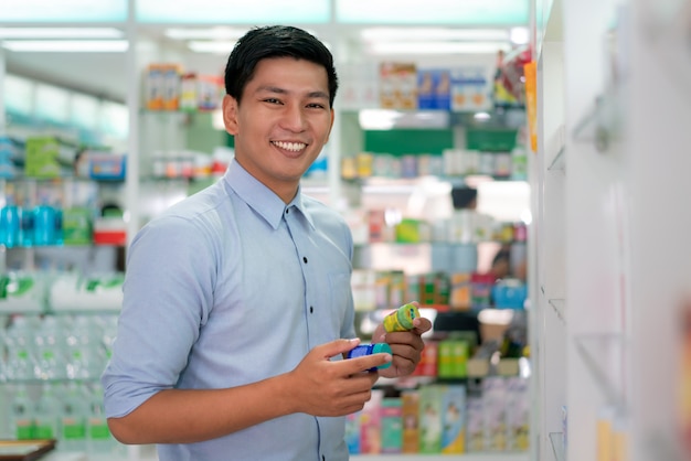 Азиатский клиент выбирая продукт и смотря камеру в аптеке фармации.