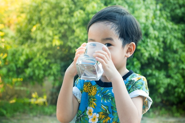 アジアのかわいい男の子飲む水健康と緑の木の背景でリフレッシュ。