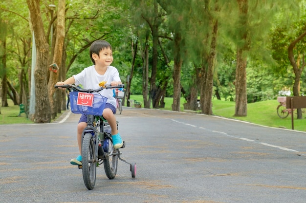 アジアのかわいい男は自転車公園緑の自然の背景に乗る