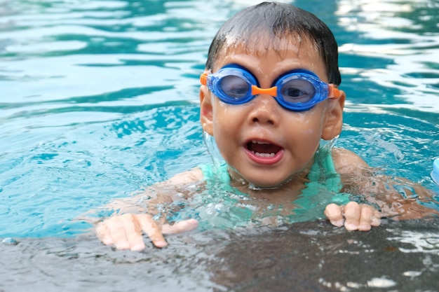 Ragazzo asiatico cute spruzzi sulla piscina di estate