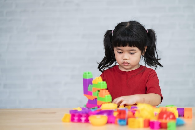 Bambina asiatica carina divertente in età prescolare in una maglietta colorata che gioca con lego o blocchi di giocattoli da costruzione che costruiscono una torre nella stanza dell'asilo o nel soggiorno bambini che giocano i bambini all'asilo