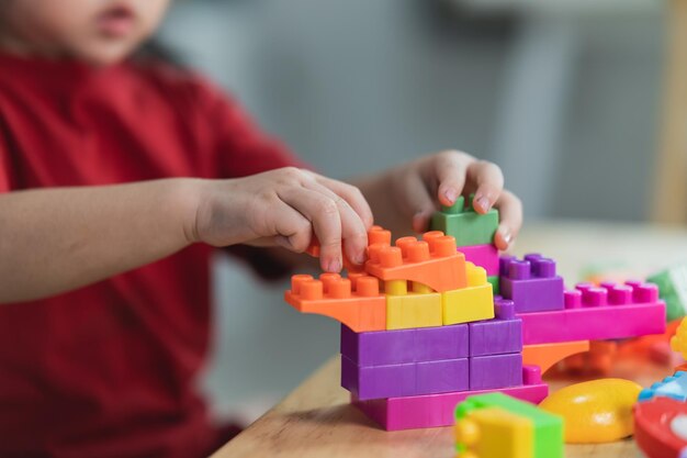 Asian cute funny preschooler little girl in a colorful shirt\
playing with lego or construction toy blocks building a tower in\
kindergarten room or living room kids playing children at day\
care