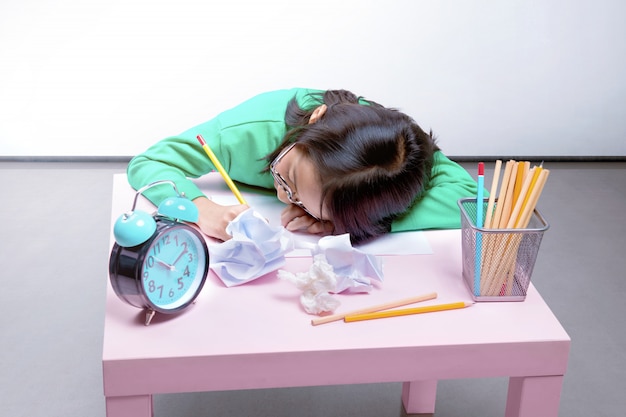 Asian cute girl in glasses fall asleep while writing on the desk 