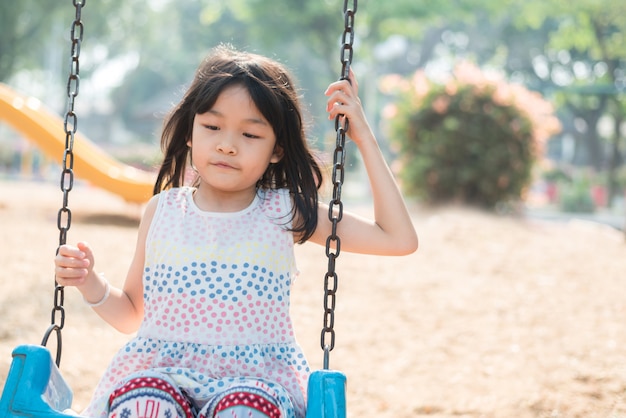 Photo asian cute girl having fun and happy on swing in playground, she is a happy and enjoyable on her holiday