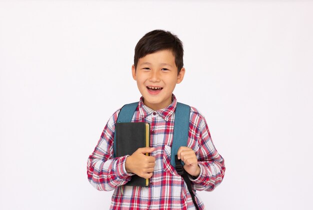 本と小さなランドセルを持って学校に行くアジアのかわいい子供の肖像画の少年、白い表面上で隔離