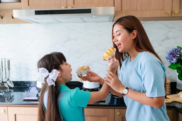 アジアのかわいいお母さんは、家族の日のために自宅のキッチンで娘に料理を教える