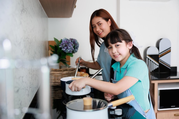 아시아의 귀여운 엄마는 가족의 날을 위해 집에서 부엌에서 음식을 요리하는 딸을 가르칩니다.