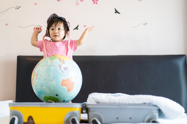 Photo asian cute smile little baby girl wearing hat standing on bed feeling funny, laughing and dancing in bedroom.