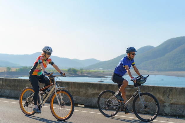 Photo asian cyclist couple riding together for exercise around the lake in the morning