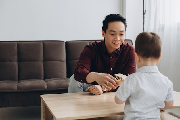 Asian dad and his cute little son playing with a wooden plane in a bright room