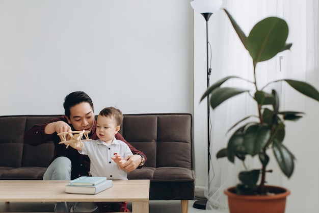 Asian dad and his cute little son playing with a wooden plane in a bright room