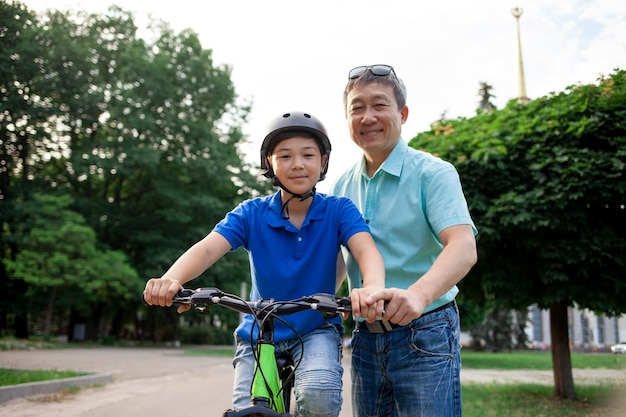 アジア人の父親が息子に自転車に乗ることを教える 韓国人のシニアが子供を助ける ヘルメットをかぶった少年が積極的にリラックスしている