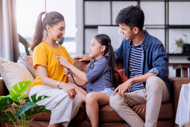 Asian daughter play doctor checking up her mother with care and happiness in living room on sofa couch at homefemale daughter playroll doctor nurse use stethoscope listen her mom heart pulse with fun