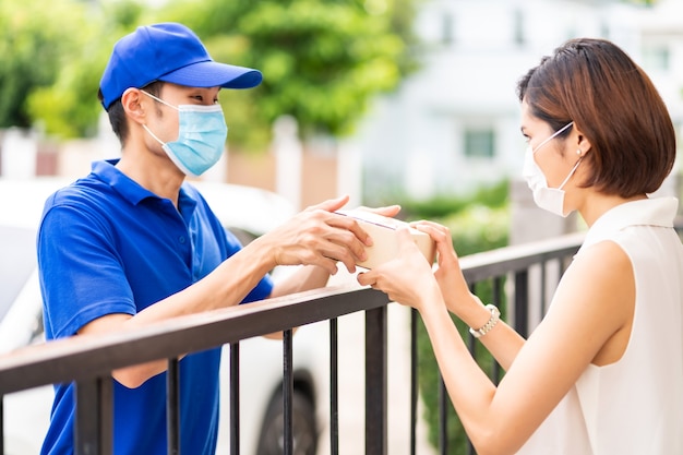 Asian consegna uomo in camicia blu che maneggia pacchetto e dà a giovane donna cliente a casa.