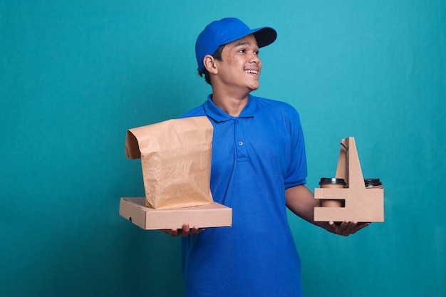 Asian delivery man in blue uniform with pizza box, food package and takeaway coffee