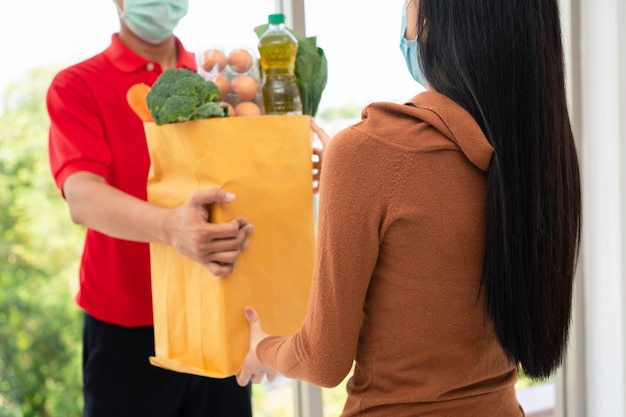 얼굴 마스크를 착용하고 신선한 음식의 가방을 들고 슈퍼마켓에서 아시아 배달 남자