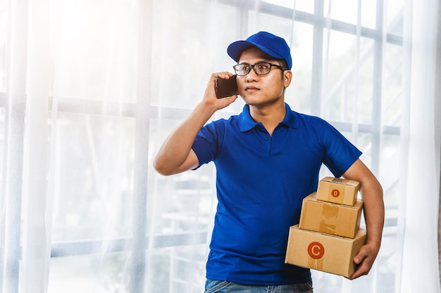 Asian delivery man holding delivery box and using cellphone while standing with parcel boxes