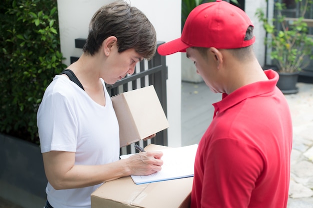 Asian delivery man in red uniform delivering parcel box to woman recipient at home