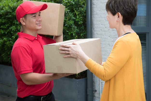 Asian delivery man in red uniform delivering parcel box to woman recipient at home