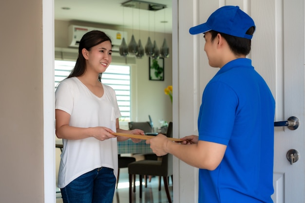 Молодой человек азиатской доставки в синей форме держит документы перед домом