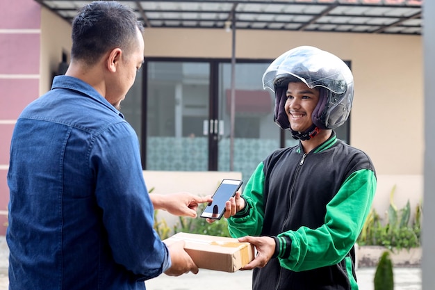 Photo asian deliveryman holding a package and phone delivery to male customer