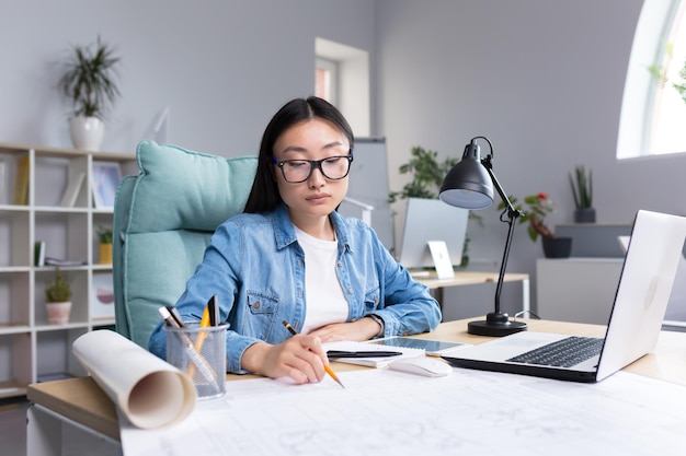 Asian designer working in office with blueprints woman at work in casual clothes