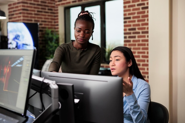 Asian developer and african american colleague developing digital art using modelling software. Creative agency production department office workers brainstorming 3D project ideas.