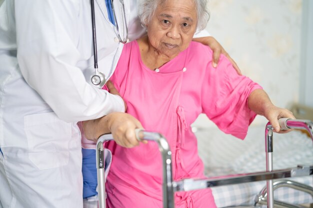 Asian doctor care help and support senior woman patient walk with walker