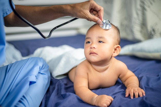 Asian Doctor examining little baby with stethoscope in clinic Baby health concept