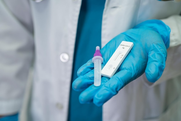 Азиатский врач в костюме СИЗ держит набор для тестирования антигена слюны для проверки коронавируса Covid19 в больнице