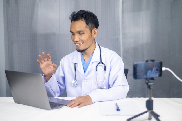 Photo asian doctor smiling male doctor sitting at table with laptop and stethoscope background medicine profession technology and people concept