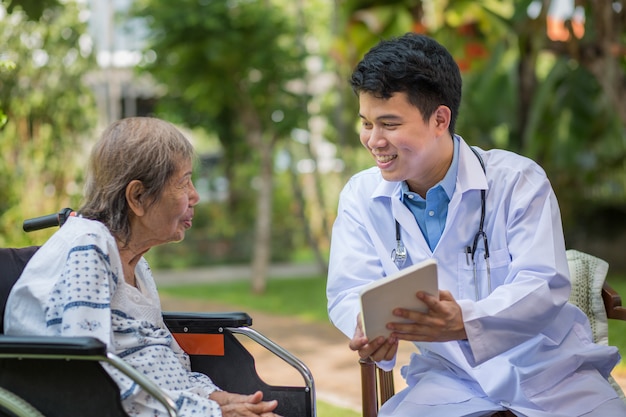 Asian doctor talking with elderly female patient on wheelchair