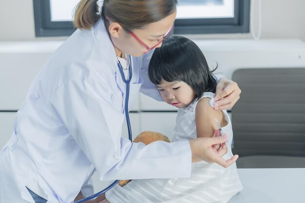 사진 청진기를 사용하여 사랑스러운 소녀의 호흡과 심장을 확인하는 아시아 의사는 어린이의 건강을 확인합니다태국 사람들