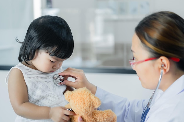 사진 청진기를 사용하여 사랑스러운 소녀의 호흡과 심장을 확인하는 아시아 의사는 어린이의 건강을 확인합니다태국 사람들