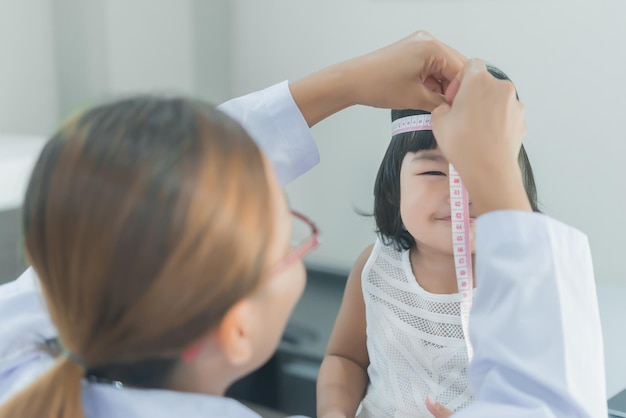 청진기를 사용하여 사랑스러운 소녀의 호흡과 심장을 확인하는 아시아 의사는 어린이의 건강을 확인합니다태국 사람들머리 크기를 측정합니다