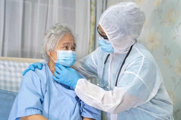 Asian doctor wearing face shield and PPE suit new normal to check patient protect safety infection Covid-19 Coronavirus outbreak at quarantine nursing hospital ward.