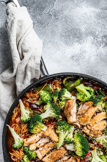 Asian egg noodles with vegetables and meat on cooking pan. Gray background. Top view. Space for text