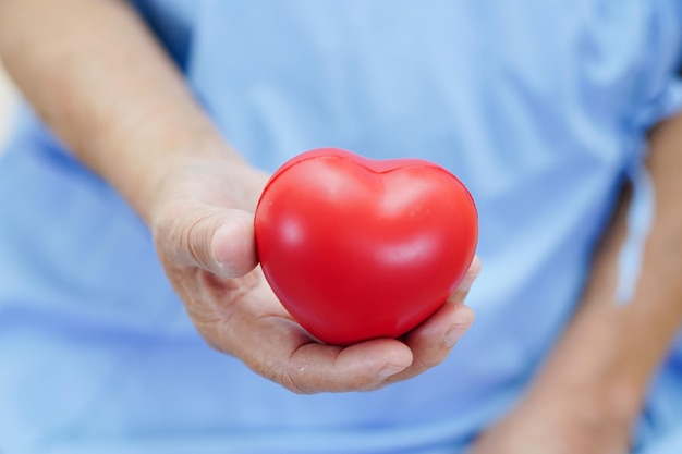 Paziente anziano asiatico della donna che tiene cuore rosso in ospedale