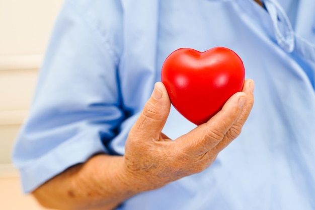 Asian elder senior woman patient holding red heart in hospital