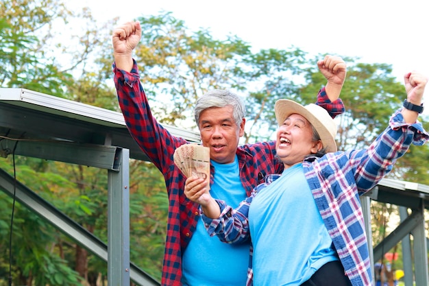 Foto coppia di anziani asiatici che coltivano l'agricoltura sorridendo felice tenendo il baht tailandese come reddito dall'agricoltura