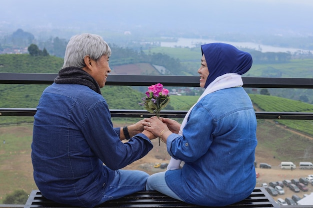 アジアの老夫婦幸せな年配のロマンチックなカップルが座って、お互いに笑って花を持っています