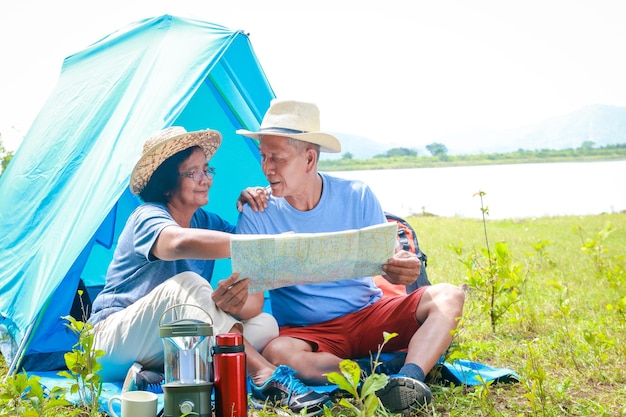 Asian elderly couple happy to travel in nature Set up a tent and camp in the forest Tourism concept of the elderly in retirement age Tourists and travelers trekking