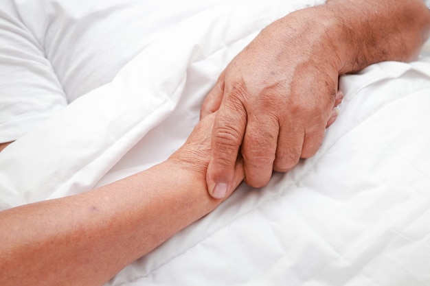 Азиатская пожилая пара спит, держась за руки в постели в спальне, концепция семьи, медицинская страховка для пожилых людей