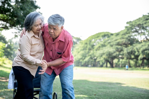 Asian elderly couple wife helping husband to get up from the wheelchair to do physical therapy