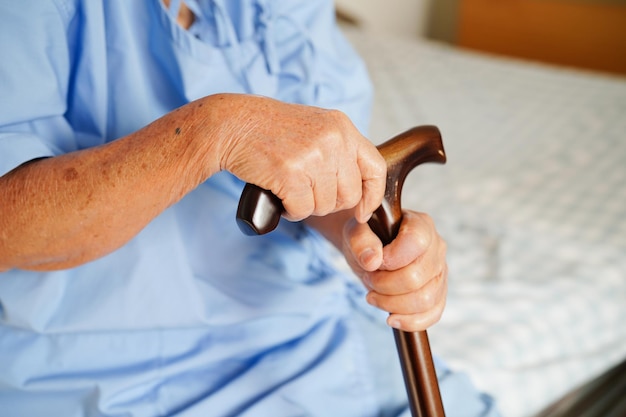 Asian elderly disability woman patient holding walking stick in wrinkled hand at hospital