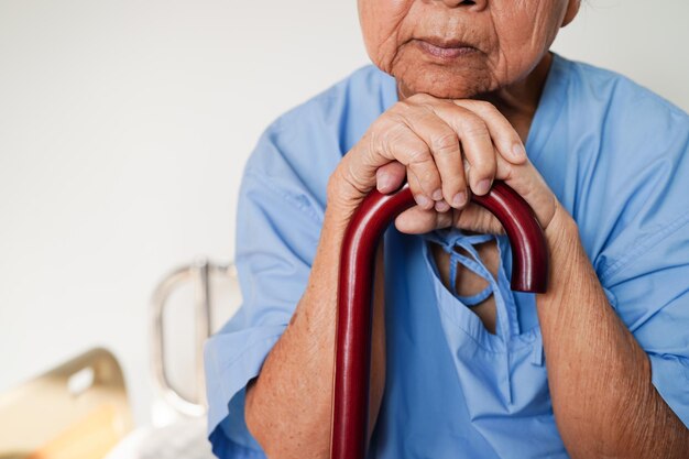 Asian elderly disability woman patient holding walking stick in wrinkled hand at hospital