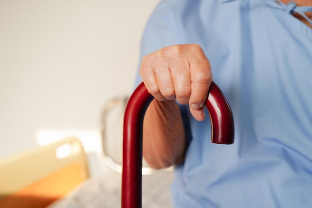 Asian elderly disability woman patient holding walking stick in wrinkled hand at hospital